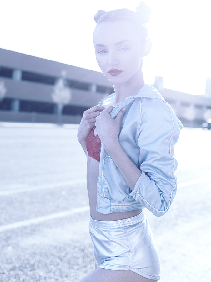 Fashion image of model Kateri Dion on the street in braided pigtails wearing a sheer lace red bralet, metallic blue vintage 80s jacket, and silver metallic disco shorts photographed by Joshua Pyles