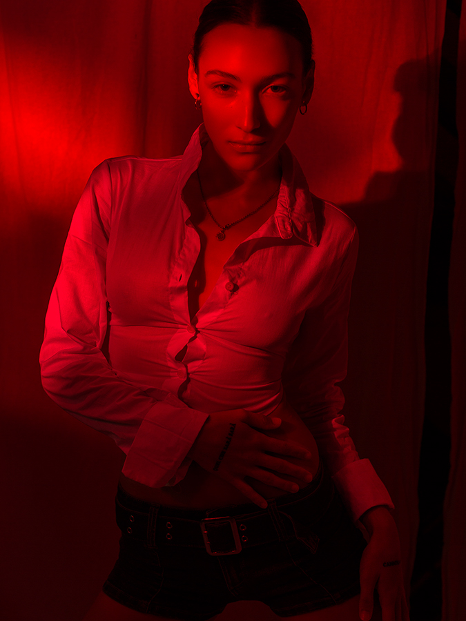 Red monochrome image of model Tehya McDonald posing in a sheer white blouse and short shorts photographed by Joshua Pyles